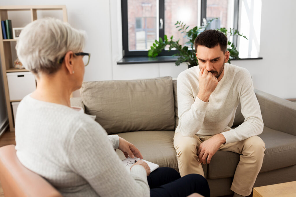 young man seated in professional office setting and talking about the benefits of cognitive-behavioral therapy for addiction recovery with an older behavioral health specialist